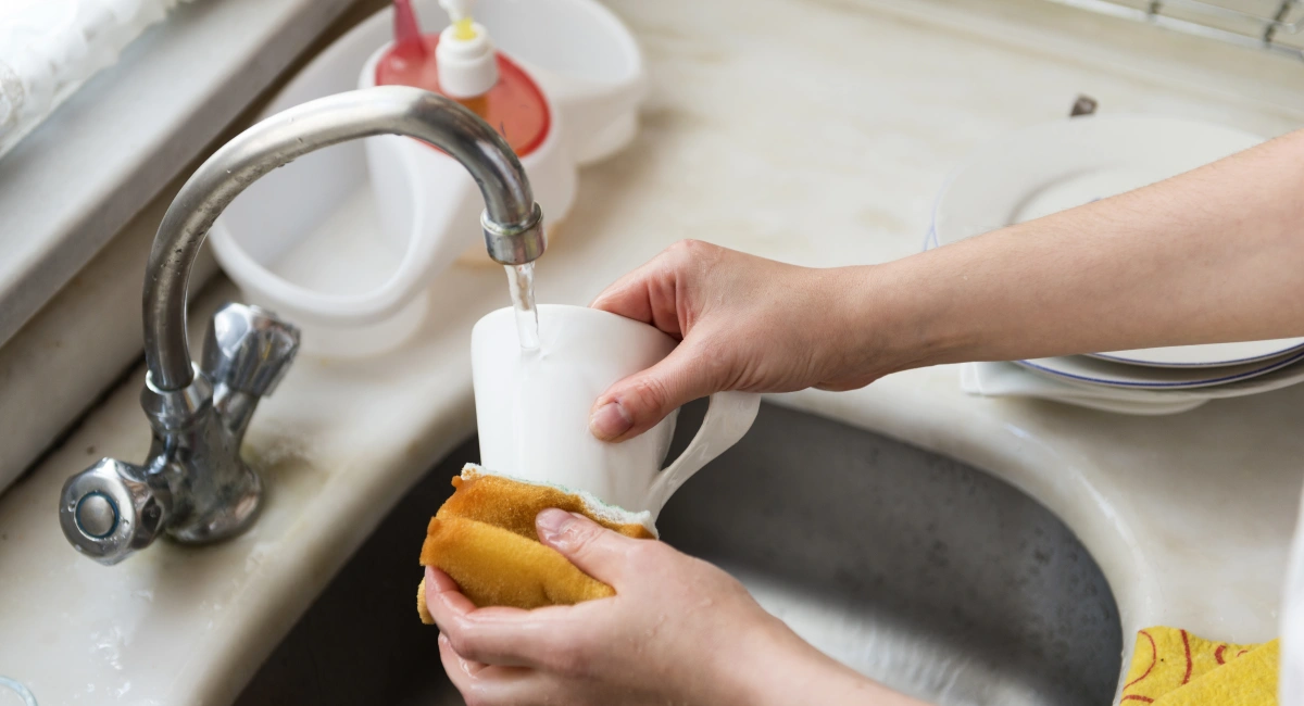 Woman handwashing mug in kitchen sink