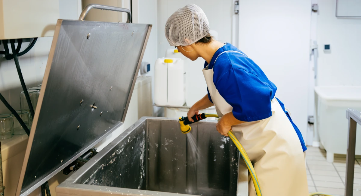 Food processing staff member cleaning and sanitizing a commercial storage using a hose in a food preparation area.